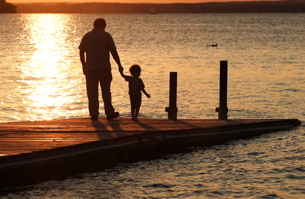 Grandfather and grandson walking on dock at sunset